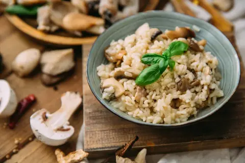 Kremowe risotto z grzybami, ozdobione listkiem bazylii. Pyszny ryż włoski w misce, otoczony świeżymi grzybami i papryczką chili.