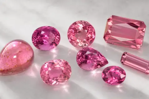 Variedad de turmalina colores rosados, desde el fucsia intenso hasta el rosa pálido, en distintas formas y cortes, brillando sobre una superficie clara.