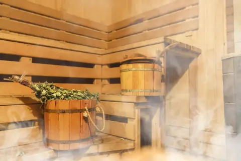 Drewniana sauna po siłowni, z parującym wiadrem i miotełką. Idealne miejsce na relaks i regenerację.