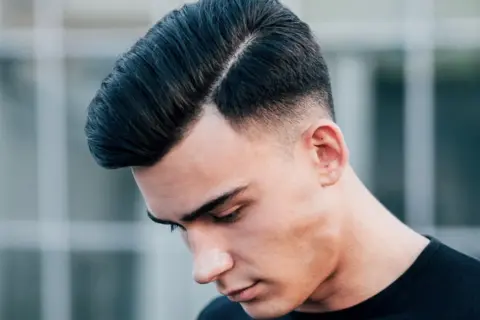 Ein Mann mit einem modernen Undercut für Herren, die Haare zur Seite gescheitelt und am Hinterkopf kurz rasiert.