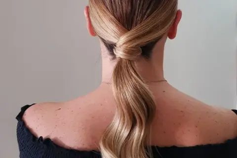 Capelli biondi raccolti in una coda bassa con un'elegante torsione, perfetta per una cerimonia.
