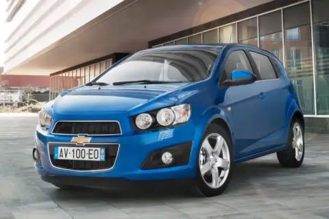 Błękitny Chevrolet Aveo stoi przed nowoczesnym budynkiem.