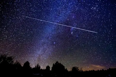 Una estrella fugaz cruza el cielo nocturno estrellado, ideal para ver las Perseidas en Madrid.