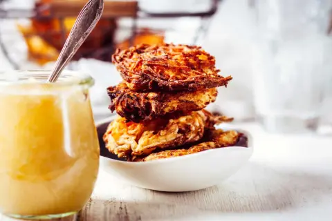 Goldbraune Kartoffelpuffer stapeln sich in einer Schüssel, daneben ein Glas Apfelmus. Ein perfektes Kartoffelpuffer Rezept für jeden Anlass.