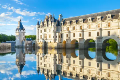 Le château de Chenonceau, joyau des monuments de la Loire, se reflète dans l'eau paisible sous un ciel bleu.