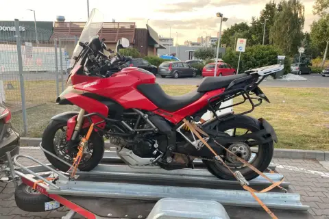 Czerwony motocykl Ducati na przyczepie, zabezpieczony pasami.