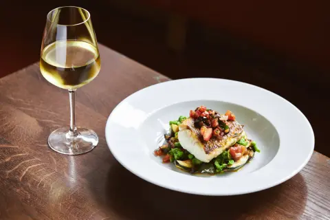 Piatto di pesce con verdure e un bicchiere di ribolla gialla.