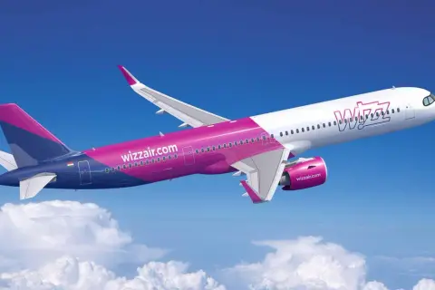 Samolot Wizz Air lecący na tle błękitnego nieba z chmurami.