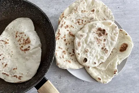 Chlebek naan przepis: świeżo usmażone placki na patelni i talerzu, gotowe do podania.
