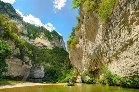 Wąwóz Gorges du Tarn, zielona rzeka i łódź z wioślarzami wśród skalnych ścian porośniętych bujną roślinnością.