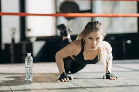 Femme faisant des pompes, un excellent exercice pour bras fripés. Elle est concentrée, dans une salle de sport.