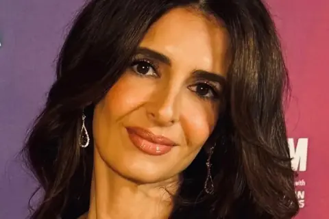 Amal Clooney, con su cabello oscuro y pendientes brillantes, sonríe ante la cámara.