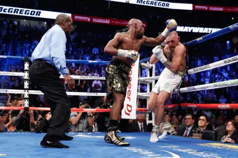 A referee watches as Floyd Mayweather Jr. lands a punch on Conor McGregor during their boxing match.