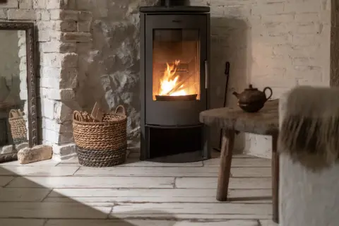 Un poêle à bois moderne diffuse une chaleur réconfortante, parfait pour un chauffage central cosy. Une théière ancienne et un panier de bois complètent l'ambiance rustique.