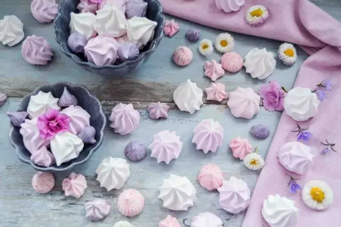 Zarte Baisers in Rosa, Lila und Weiß, perfekt für ein süßes Baiser Rezept. Kleine Blumen schmücken die Leckereien.