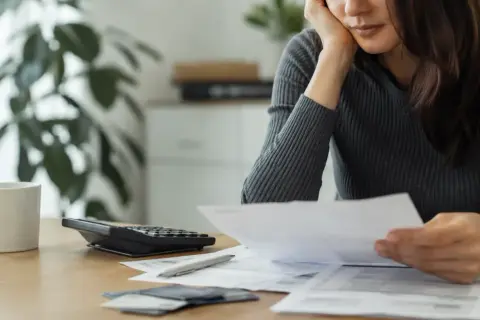 En person sitter vid ett bord med papper, en kalkylator och en kaffekopp. Kanske funderar personen på sitt skuldebrev för bolån.