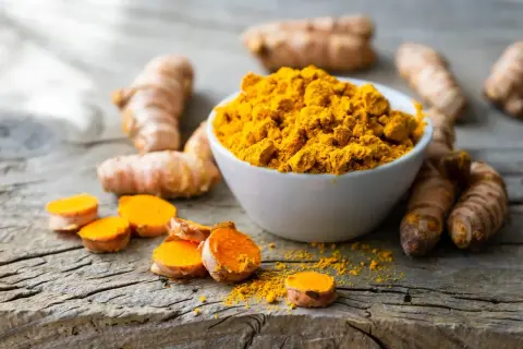 Kurkuma-Wurzeln und Pulver auf Holz. Informiert über die Frage: wieviel curcumin pro tag.