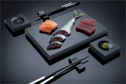 Sashimi-Zutaten: Lachs, Thunfisch, Makrele, Wasabi und Stäbchen. Die Frage "aus welchem Land kommt Sushi" führt uns nach Japan.