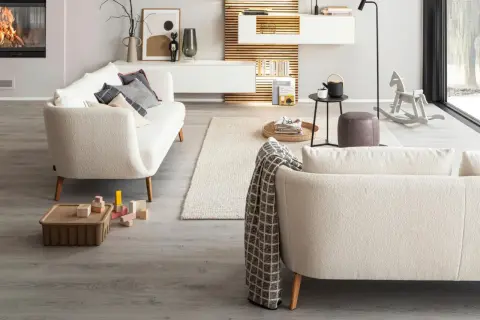 Gemütliches Wohnzimmer mit einem cremefarbenen Sofa vor bodentiefen Fenstern. Ein Kaminfeuer wärmt den Raum.