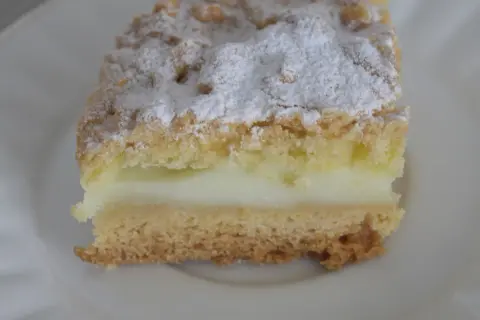 Kawałek ekspresowego kruchego ciasta z budyniem, posypana cukrem pudrem. Idealne na szybką przekąskę.