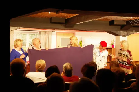 Schauspieler des losemund theater halten ein lila Tuch, während sie vor einem Publikum auftreten.