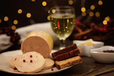 Un délicieux bloc de foie gras tranché, servi avec du pain d'épices et un verre de vin blanc, le tout dans une ambiance festive.