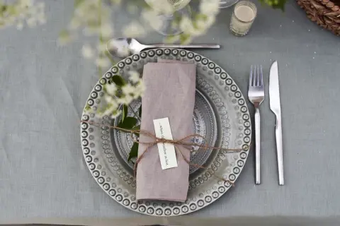 Vackert dukat bord med en lila servett vikt som en blomma, knuten med snöre. En liten lapp med texten "...when the weather is hot" sitter fäst.