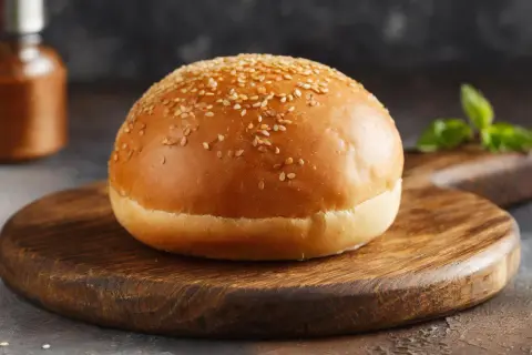 Ein goldbrauner Burger-Bun mit Sesam bestreut, liegt auf einem rustikalen Holzbrett.