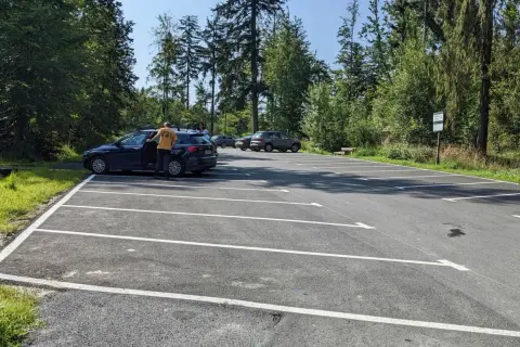 Parking przy szlaku na przełęcz Szarcula. Kilka samochodów na nowym, asfaltowym parkingu otoczonym lasem.