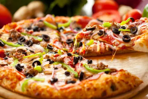 Pyszna pizza na gotowym spodzie z serem, oliwkami, papryką i salami. Ciągnący się ser zachęca do spróbowania.