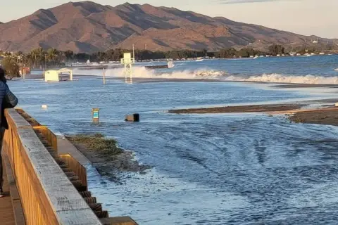 El espigón Garrucha bajo el agua, con olas rompiendo y montañas al fondo.