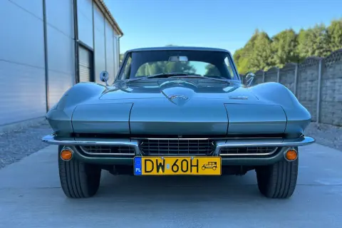 Klasyczny zielony Corvette C2 z lat 60. stoi przed nowoczesnym budynkiem.