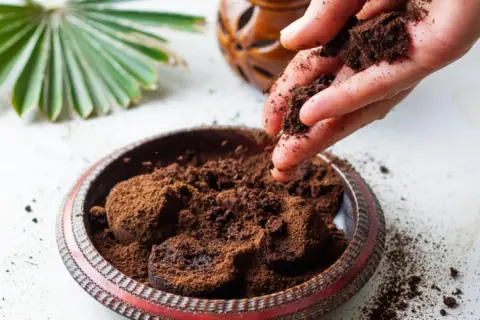 Mano esparciendo posos de café en un cuenco decorativo. El café molido se acumula en el cuenco, listo para ser reutilizado.