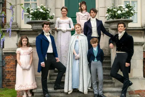 Die Bridgerton-Familie posiert vor ihrem Anwesen. Die Kinder, von jung bis erwachsen, tragen prächtige Kleider und Anzüge.