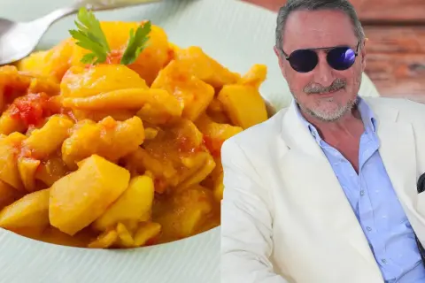 Un hombre con gafas de sol y traje blanco sonríe junto a un plato de papas con choco de la abuela, un guiso casero.