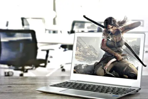 Lara Croft, postać z gry komputerowej, wychodzi z ekranu laptopa, gotowa do akcji z łukiem i czekana.