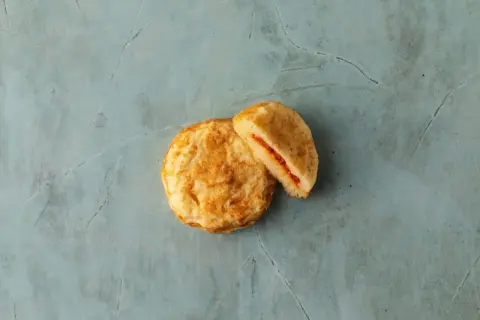 Två gyllene plättar, en hel och en delad, med en röd fyllning. Perfekta pannkakor för frukost eller fika.