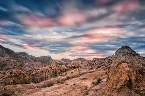 Paisaje desértico con formaciones rocosas y un cielo dramático al atardecer, evocando la belleza del volcan Almería.