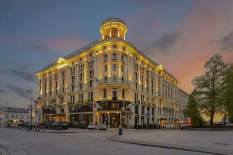 Elegancki budynek Mercure Warszawa Centrum oświetlony wieczorem, z charakterystyczną wieżyczką i ozdobną fasadą, na tle zachodzącego słońca.
