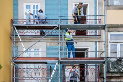 Trabajadores en andamios renuevan fachadas de edificios, cumpliendo la normativa sobre estética fachadas de edificios.