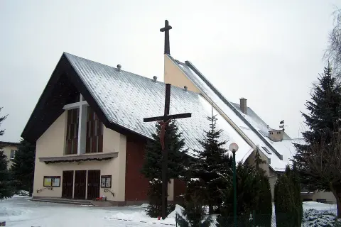 Kościół w Robakowie zimą, pokryty śniegiem, z krzyżem przed fasadą.