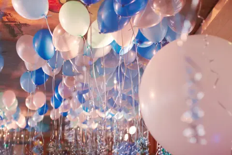 Une multitude de ballons bleus, blancs et roses flottent au plafond, prêts à être gonflés pour une fête.