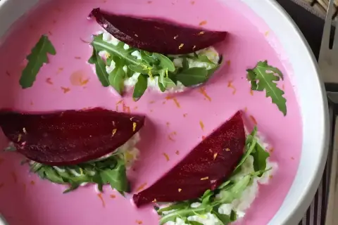 Vacker vegetarisk mat: rödbetor, ruccola och färskost i en rosa soppa, garnerad med rivet citronskal.