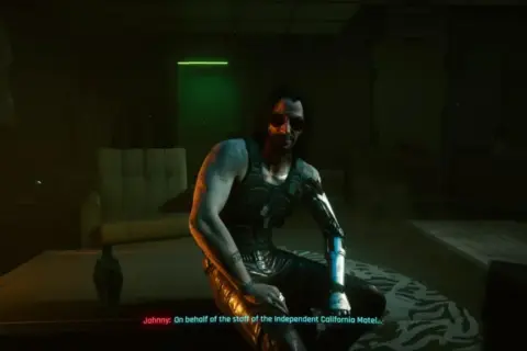 Johnny Silverhand z Cyberpunk 2077 w mrocznym pokoju, z cybernetycznym ramieniem i w okularach przeciwsłonecznych.