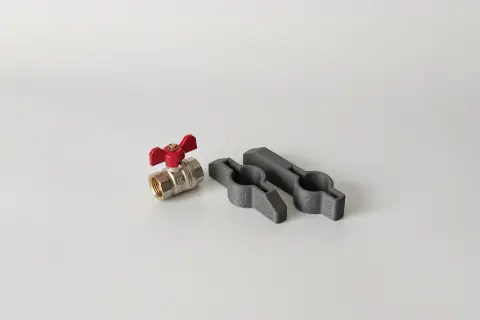 Metalowy zawór z czerwoną rączką i dwa szare uchwyty, które pomogą, jak odkręcić zapieczony zawór wody.