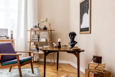 Stylowe wnętrza retro: fioletowy fotel, drewniany stolik z popiersiem i książkami, regał pełen literatury, gramofon i mapa na ścianie.