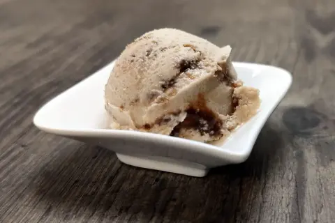 Ein Löffel cremiges Tiramisu Eis mit dunklen Schokoladenstreifen in einer weißen Schale auf Holzhintergrund.
