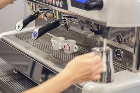 Mano che prepara un caffè con la bar macchina caffè. Due tazzine bianche attendono il loro turno.