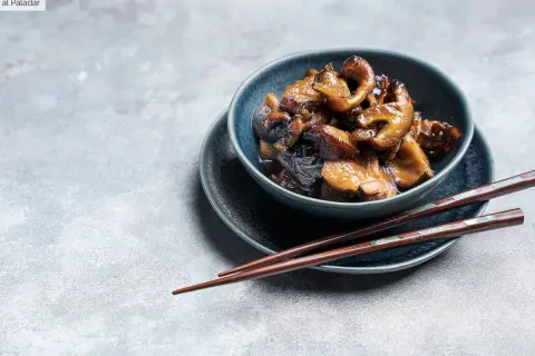 Deliciosas setas shiitake salteadas en un cuenco azul, listas para ser disfrutadas con palillos.