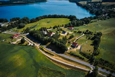 Malownicze **trasy rowerowe Mazury** wiodą przez zielone pola i lasy, w pobliżu błękitnego jeziora.